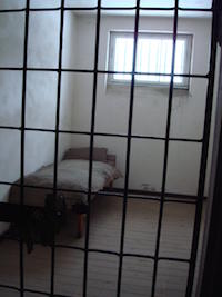 Empty cot inside a prison cell seen through the bars.