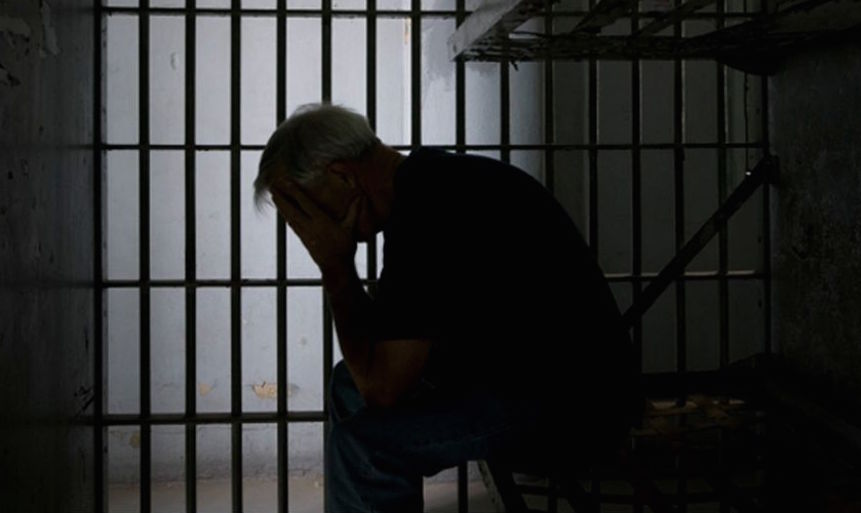 Inmate in despair, sitting in dark cell with head held in hands.