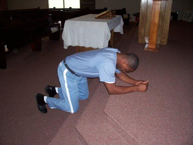 Prisoner kneeling and praying in a prison chapel.