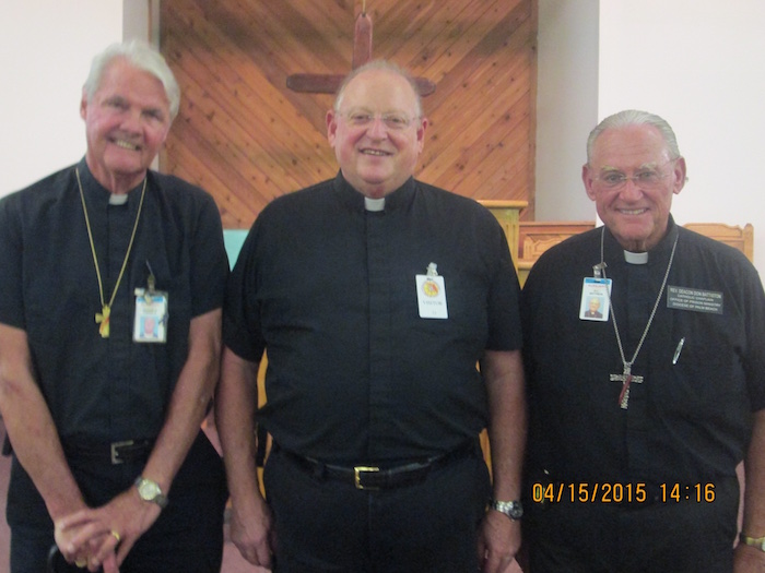 Three Deacons posing for a picture in front of a cross inside a church.