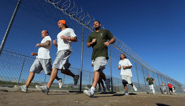 Inmates jogging along a razor wire fence.
