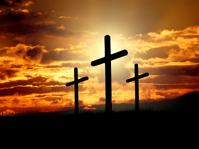 Three empty crosses standing in stark contrast to the dark orange sunset in the background.