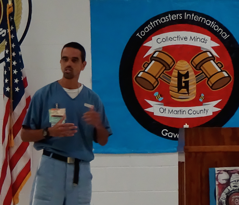 Inmate delivering a speech, the Toastmasters logo in the background.
